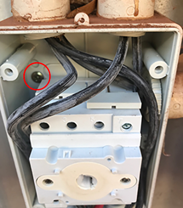 The photo shows a DC isolator with the front cover open. A red circle shows a self-tapping screw drilled through the back of the isolator casing.