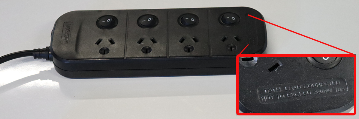 The image shows a black colour four outlet domestic power board. The insert shows a closer up of the section of the power board that displays the power boards capacity.
