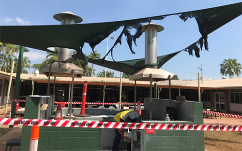 The image shows the in built barbecue for incident 2. Red hazard tape surrounds the barbecue area. The shade cloth above the barbecue area has been burnt. A one meter high wall almost encloses the barbecue area.