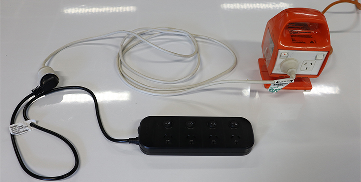The image shows a power board plugged into an extension cord, which in turn has been plugged into an outlet on an outlet box.