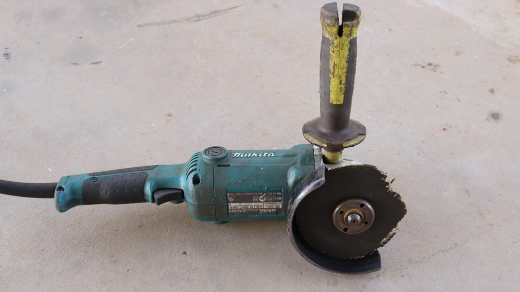 The image shows the angle grinder used in incident one on the ground. The attached cutting disc is broken with parts of the disc missing.