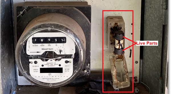 The image is of the inside of a meter box showing an old style dial meter on the left and a damaged fuse holder on the right which has exposed lived parts.