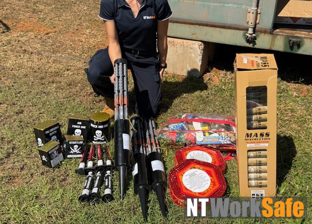 Half of the seized fireworks pictured are illegal in the Northern Territory. The photo shows an assortment of fireworks, half which are illegal, laying on the ground. A WorkSafe Inspector in kneeling on the ground next to the fireworks.