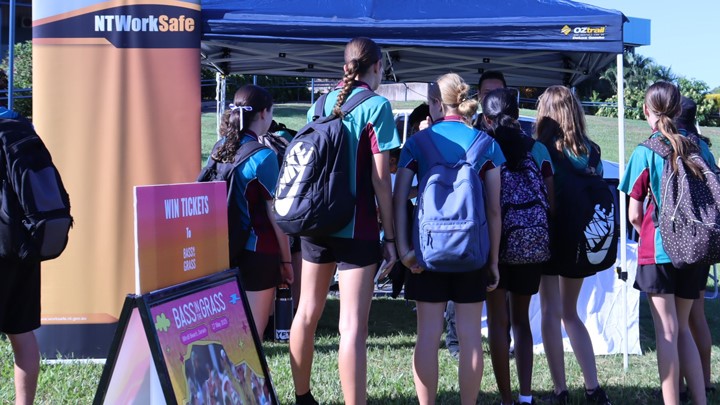 The image shows young students engaging with NT WorkSafe staff